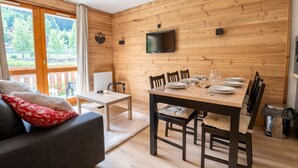 Een gezellige kamer met houten inrichting, een eettafel gedekt voor vier personen en een televisie aan de wand.