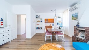 Un salon moderne avec un plancher en bois, un coin repas avec une table en bois et des chaises blanches, un canapé bleu et une cheminée.