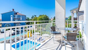 Un balcon avec une piscine, une balustrade blanche et des chaises en osier.
