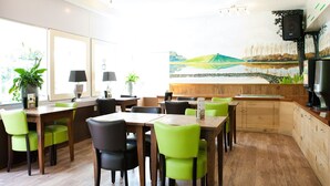 A dining area with wooden tables and chairs, potted plants, and a large painting on the wall. - Cozy Tent Lodge With Pool (Noord-Scharwoude)