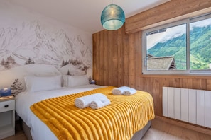 A bedroom with a bed, a wooden headboard, a window with a view of mountains, and a hanging light fixture.