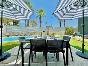 Un patio con piscina, mobiliario exterior y sombrillas.