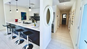 A modern kitchen with bar stools, pendant lighting, and a large mirror. - New! Audrey's Luxury Retreat - Walk Downtown (Palm Springs)