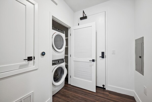 A laundry room with a washing machine and dryer, a white door with a window, and a vent on the wall.