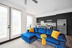 A modern living room with a blue sectional sofa, a glass coffee table, and a yellow vase.