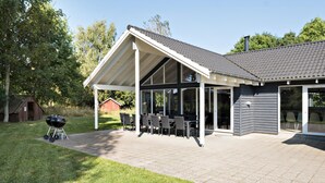 Een overdekt terras met buitenmeubelen en een barbecue.