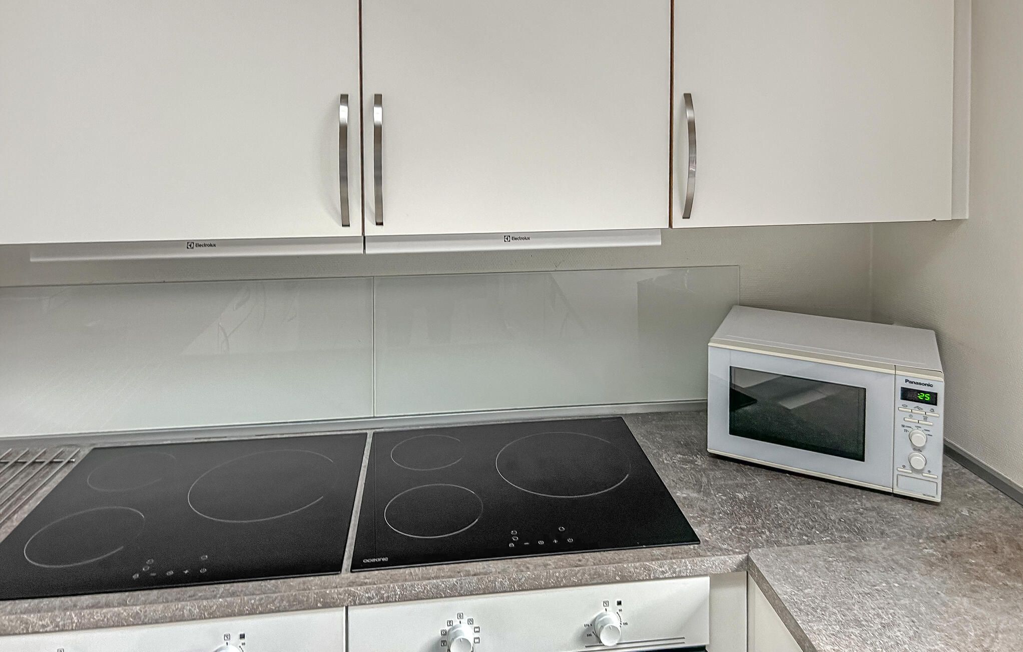A kitchen with a built-in induction cooktop, a microwave, and white cabinets.