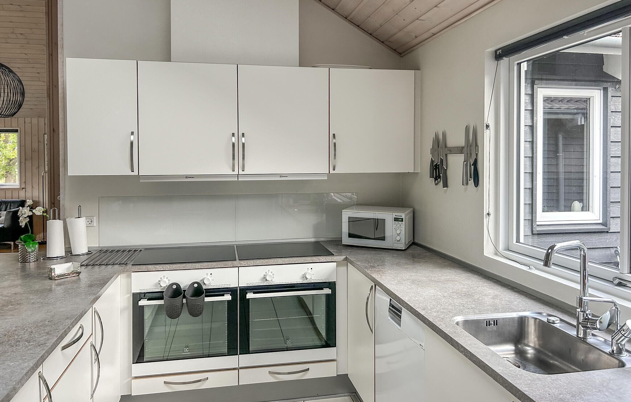 Eine moderne Küche mit weißen Schränken, einem eingebauten Backofen, einer Mikrowelle und einem großen Fenster, das für natürliches Licht sorgt.