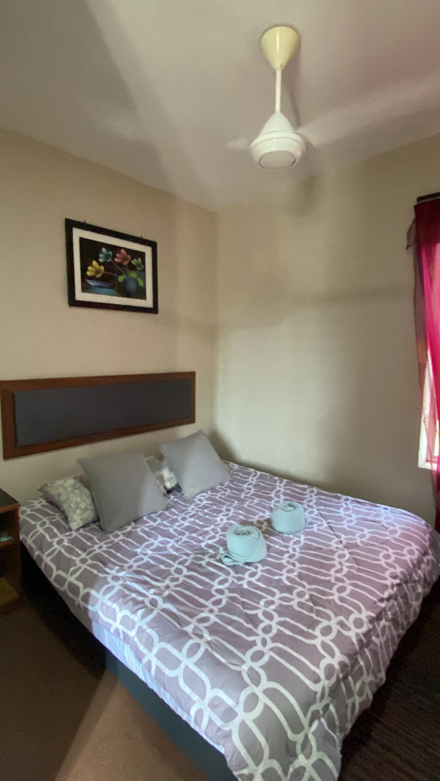 A bedroom with a bed, pillows, a ceiling fan, a framed picture, and a window with curtains.