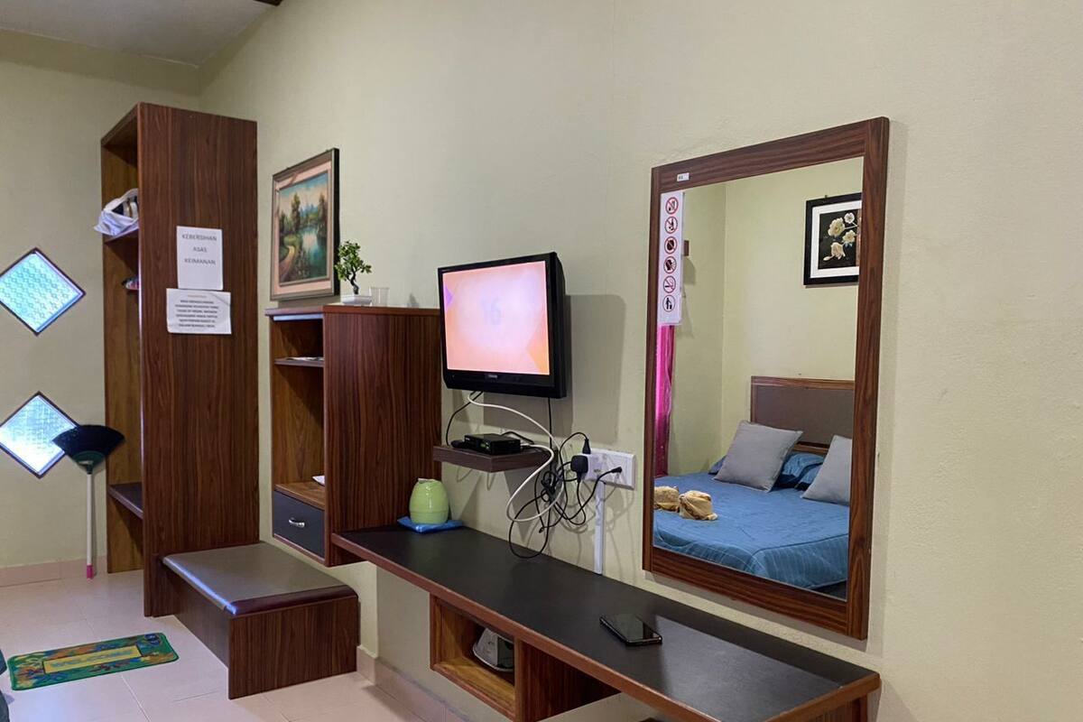Ein Schlafzimmer mit einem Bett, einem Schreibtisch mit Computer, einem Spiegel und einem Kleiderschrank.