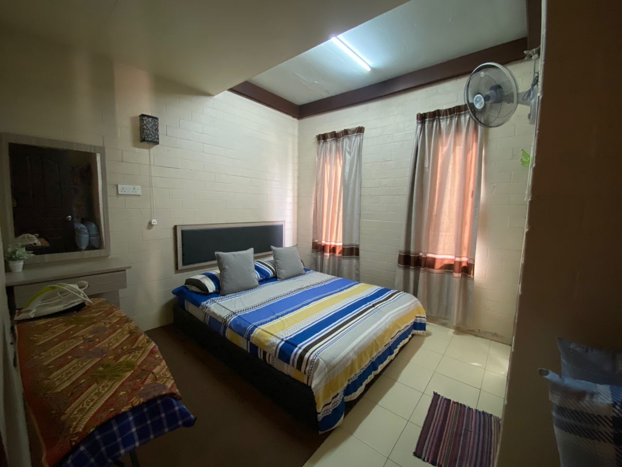A bedroom with a bed, a bedside table, a mirror, a window with curtains, and a ceiling fan.