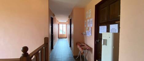 A narrow hallway with a wooden railing, a tiled floor, and a refrigerator on the right.
