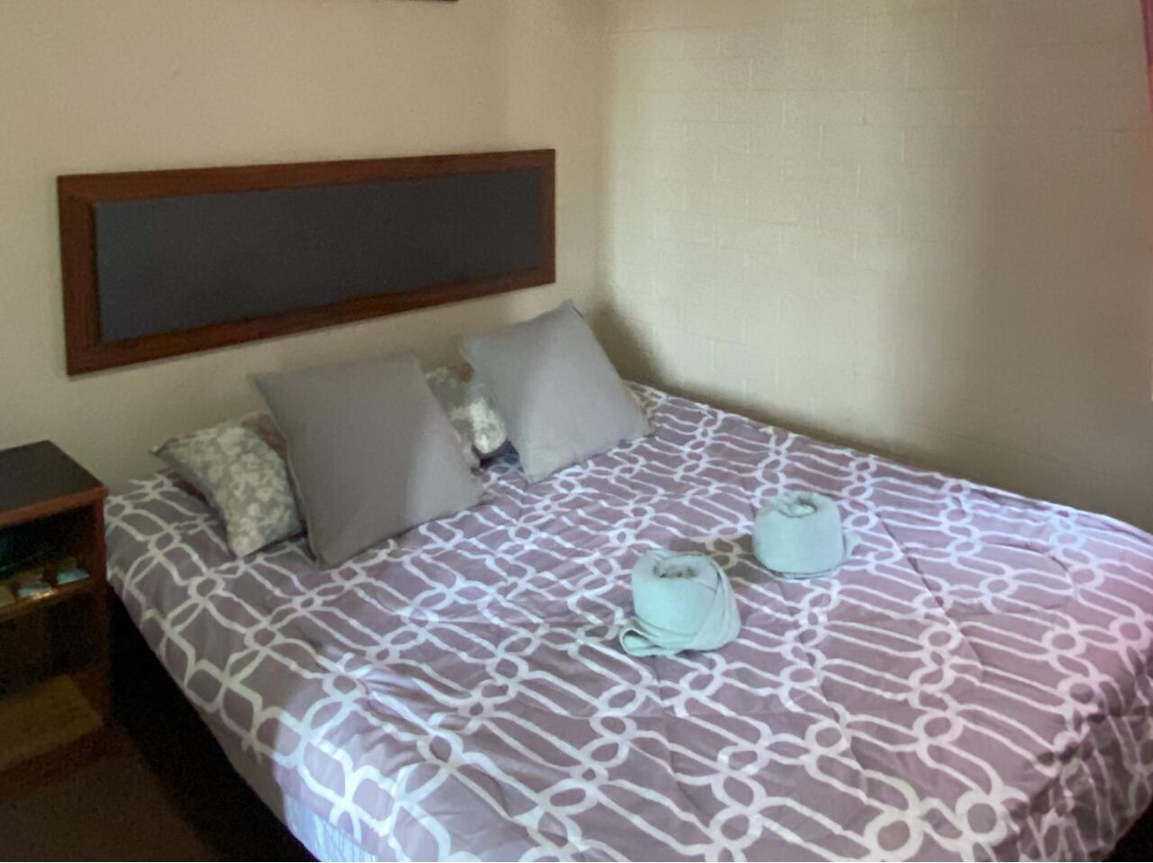 Un lit bien fait, recouvert d’une couvre-lit à motifs, avec deux oreillers et deux tables de chevet dotées de lampes.