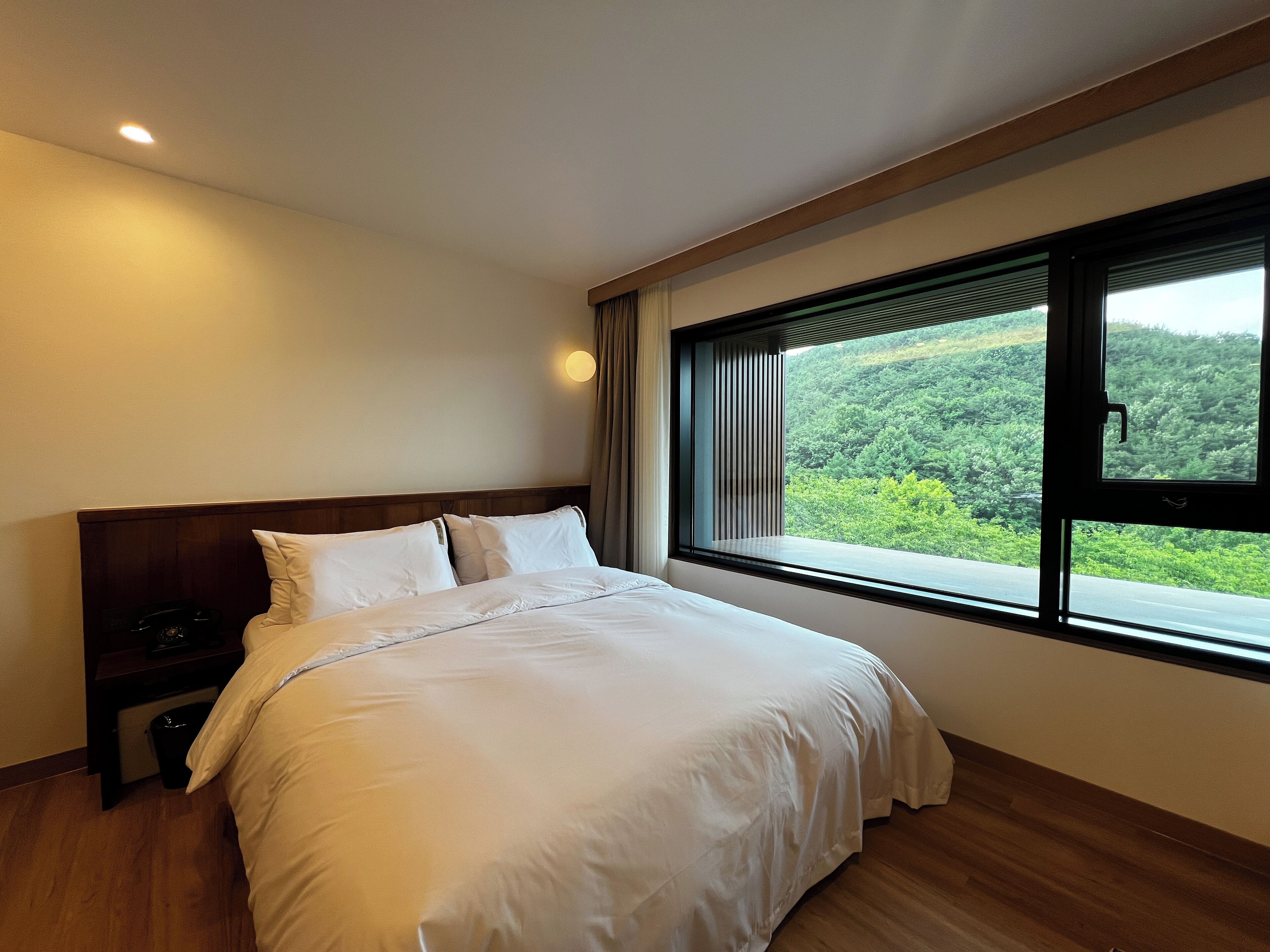 Un dormitorio con una cama grande, una mesita de noche y una ventana con vistas a zonas verdes.