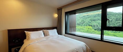 Un dormitorio con una cama grande, una mesita de noche y una ventana con vistas a zonas verdes.