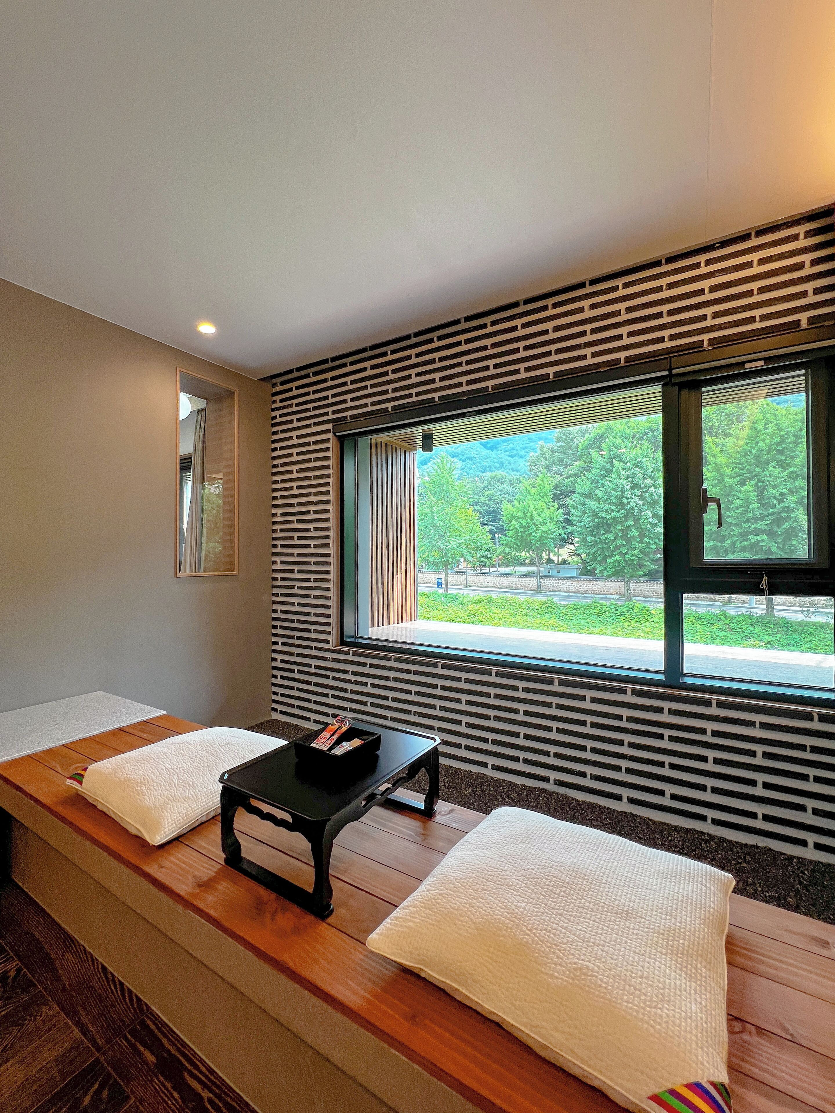 Una habitación con dos camillas de masaje, una mesita negra con revistas y una ventana con vistas a zonas verdes.