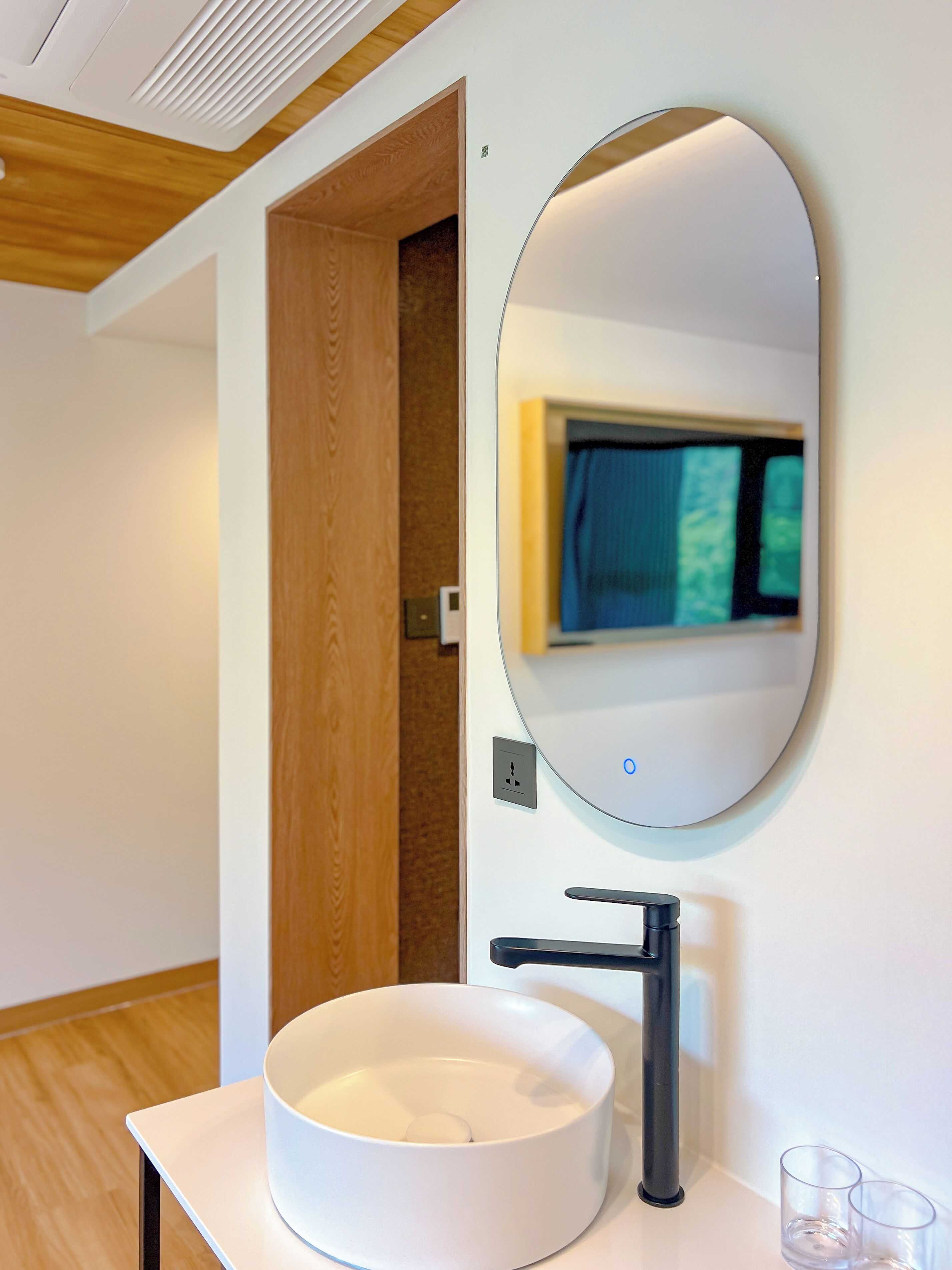 A modern bathroom with a white sink, a round mirror, and a wooden door.
