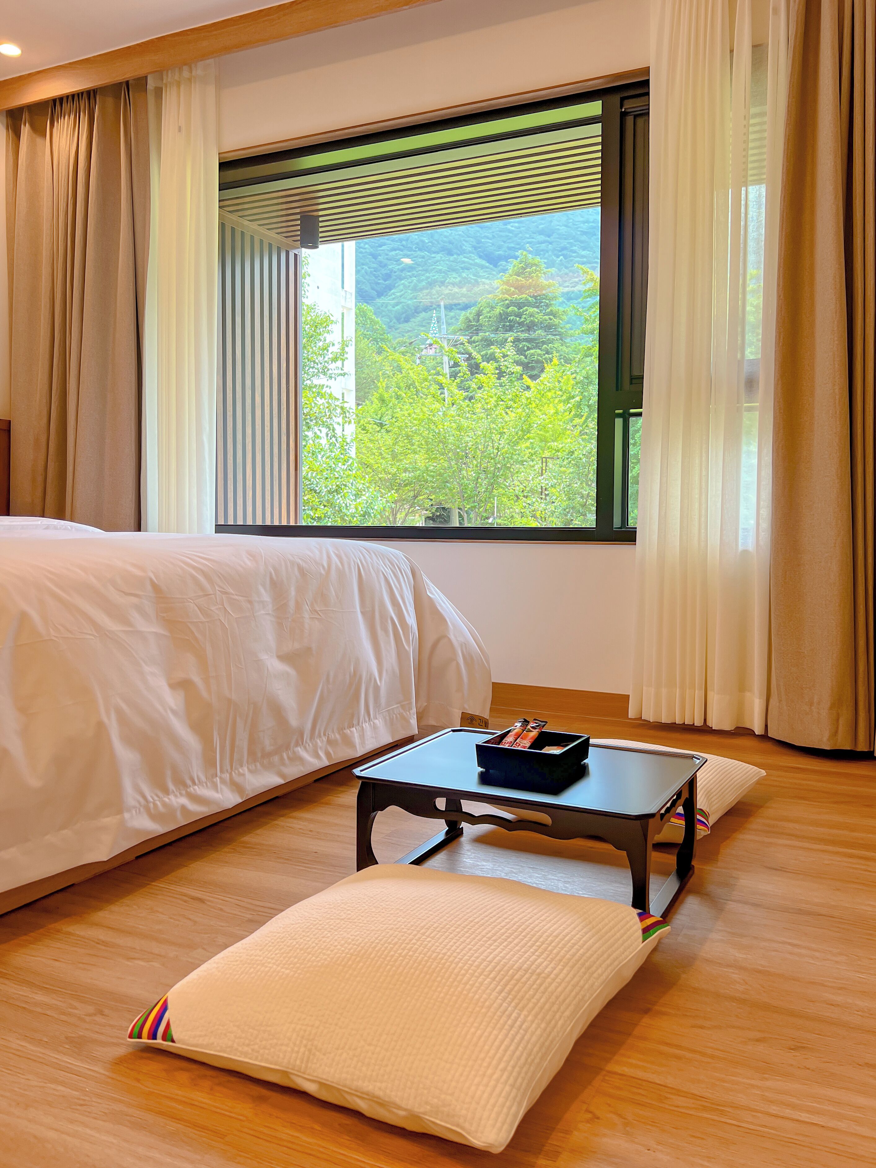 Un dormitorio con cama, una mesita con bandeja y vistas a la vegetación por la ventana.