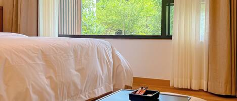 Un dormitorio con cama, una mesita con bandeja y vistas a la vegetación por la ventana.