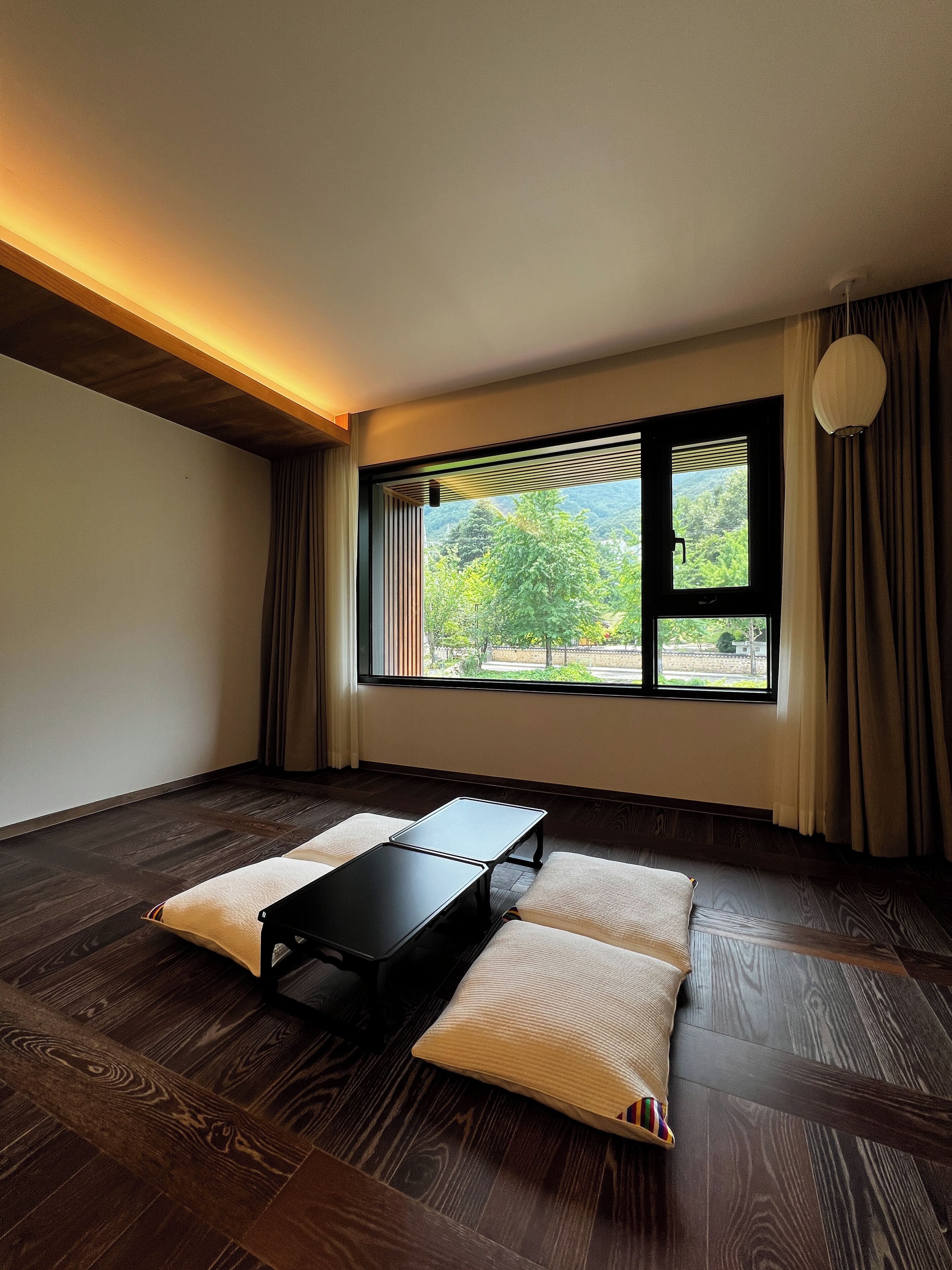 A room with a wooden floor, a black table, and a view of greenery outside.
