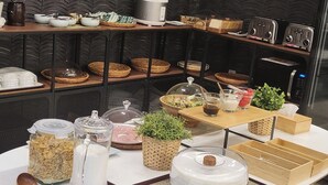 A buffet setup with various food items, including cereal, milk, and a salad, on a table with a woven placemat. - HOTEL KANWOLGE (Ulsan)