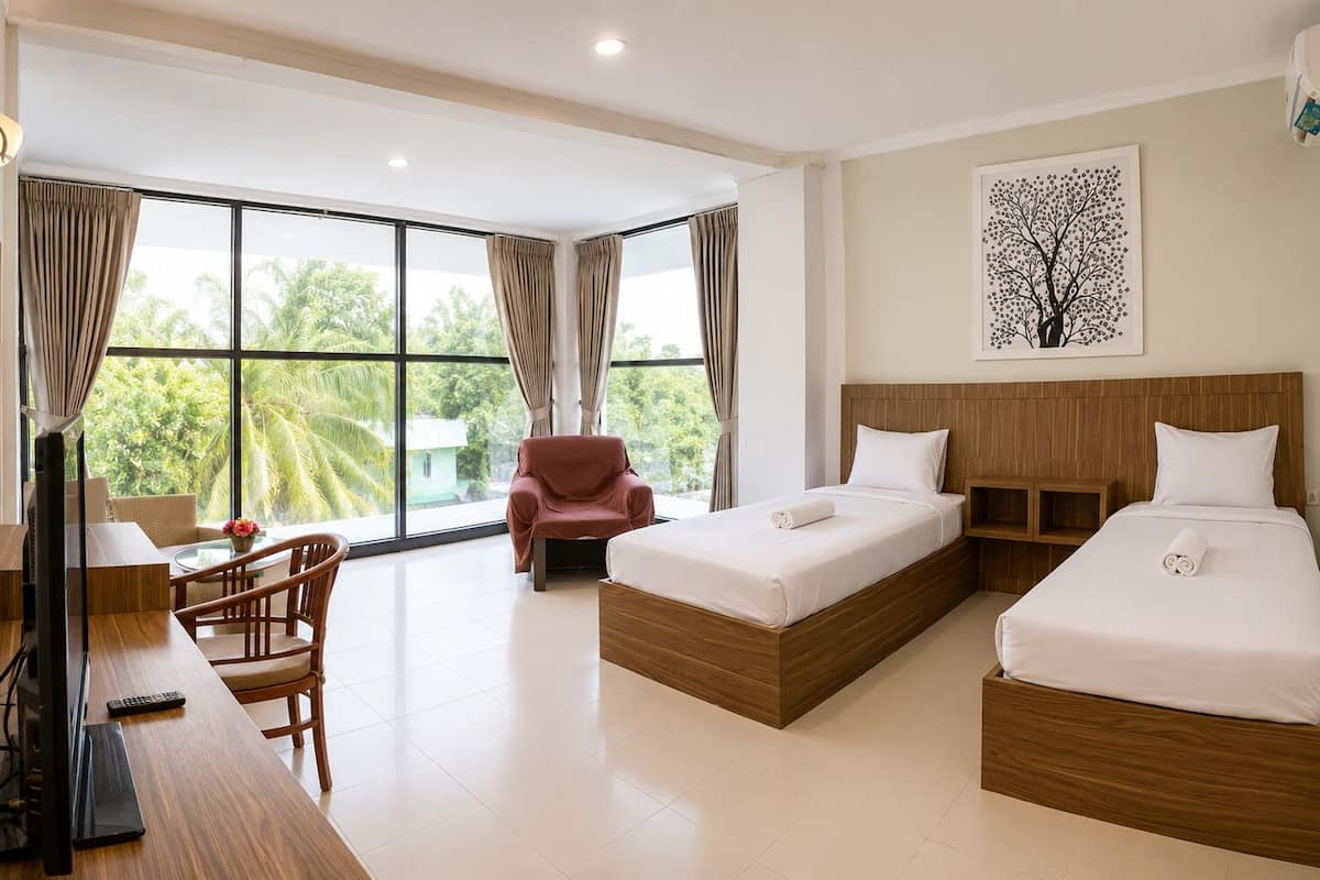 A hotel room with two beds, a desk with a chair, a TV, and large windows with curtains.