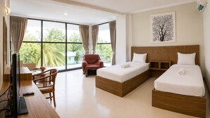 Une chambre d’hôtel avec deux lits, un bureau avec une chaise, une télévision et de grandes fenêtres avec des rideaux.