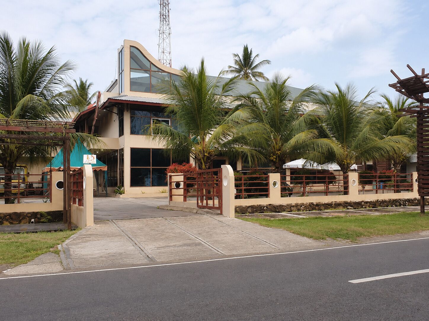 Un edificio moderno con fachada de vidrio curva, palmeras y una entrada porticada.