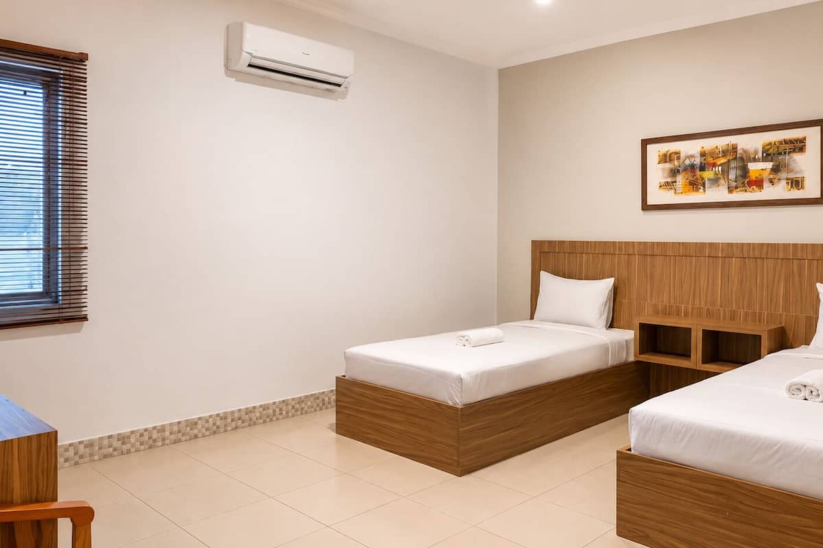 A hotel room with two wooden beds, a wooden headboard, a tiled floor, a window with blinds, and an air conditioning unit.