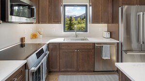 A modern kitchen with dark wooden cabinets, stainless steel appliances, and a window with a mountain view. - Cozy Guest House In The Chugach Mountains  (Anchorage)