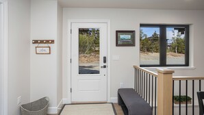A clean, modern entryway with a white door, a bench, a basket, and a framed picture on the wall. - Cozy Guest House In The Chugach Mountains  (Anchorage)