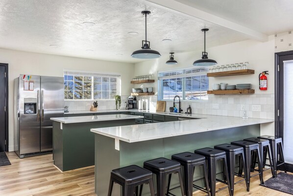 A modern kitchen with a large island, bar stools, and a stainless steel refrigerator.