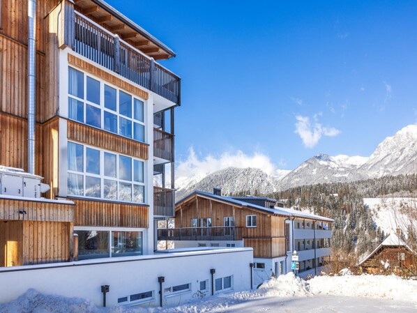 A multi-story hotel with wooden exterior and large windows, set against a snowy mountain backdrop.