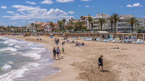 Une plage avec des transats et des parasols, un rivage sablonneux et des bâtiments en arrière-plan.