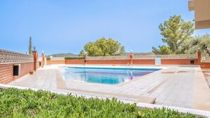 Une piscine à l’eau d’un bleu limpide, entourée d’un mur de briques et d’une clôture blanche. On aperçoit des arbres et une montagne au loin.