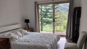 A bedroom with a bed, a chair, a lamp, and a view through a glass door. - Private cottage on 40 acres with private creek and spectacular views.  (Eden Creek)