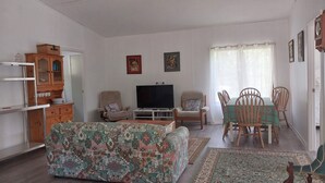 A living room with a sofa, TV, wooden cabinet, and a dining area with chairs and a table. - Private cottage on 40 acres with private creek and spectacular views.  (Eden Creek)