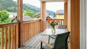 Eine Holzdiele mit Tisch und Stühlen, eine Vase mit Blumen und Blick auf Häuser und Berge.