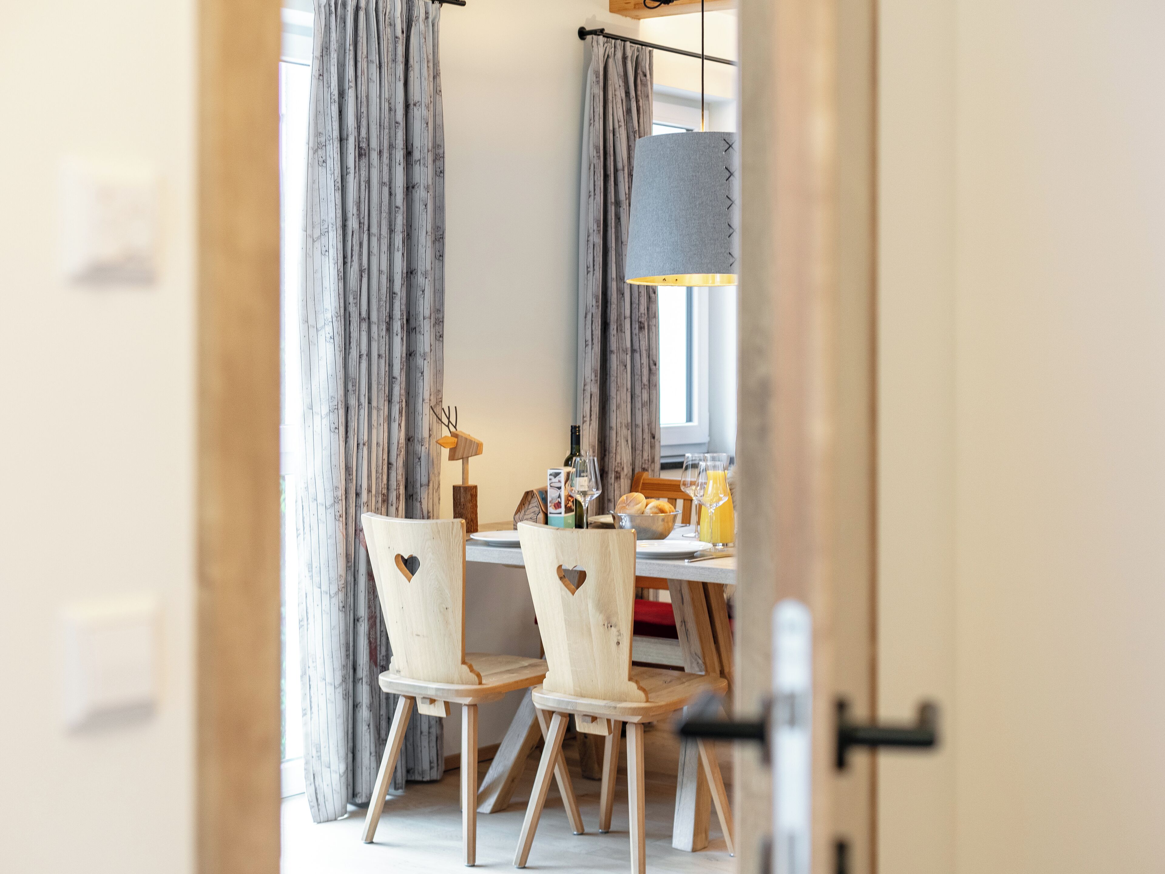 Un coin repas avec des chaises en bois, une table dressée avec des verres, une bouteille et un saladier rempli de fruits.
