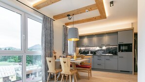 Eine moderne Küche mit grauen Schränken, ein Essbereich mit Holzkästen und ein großes Fenster mit Blick ins Freie.