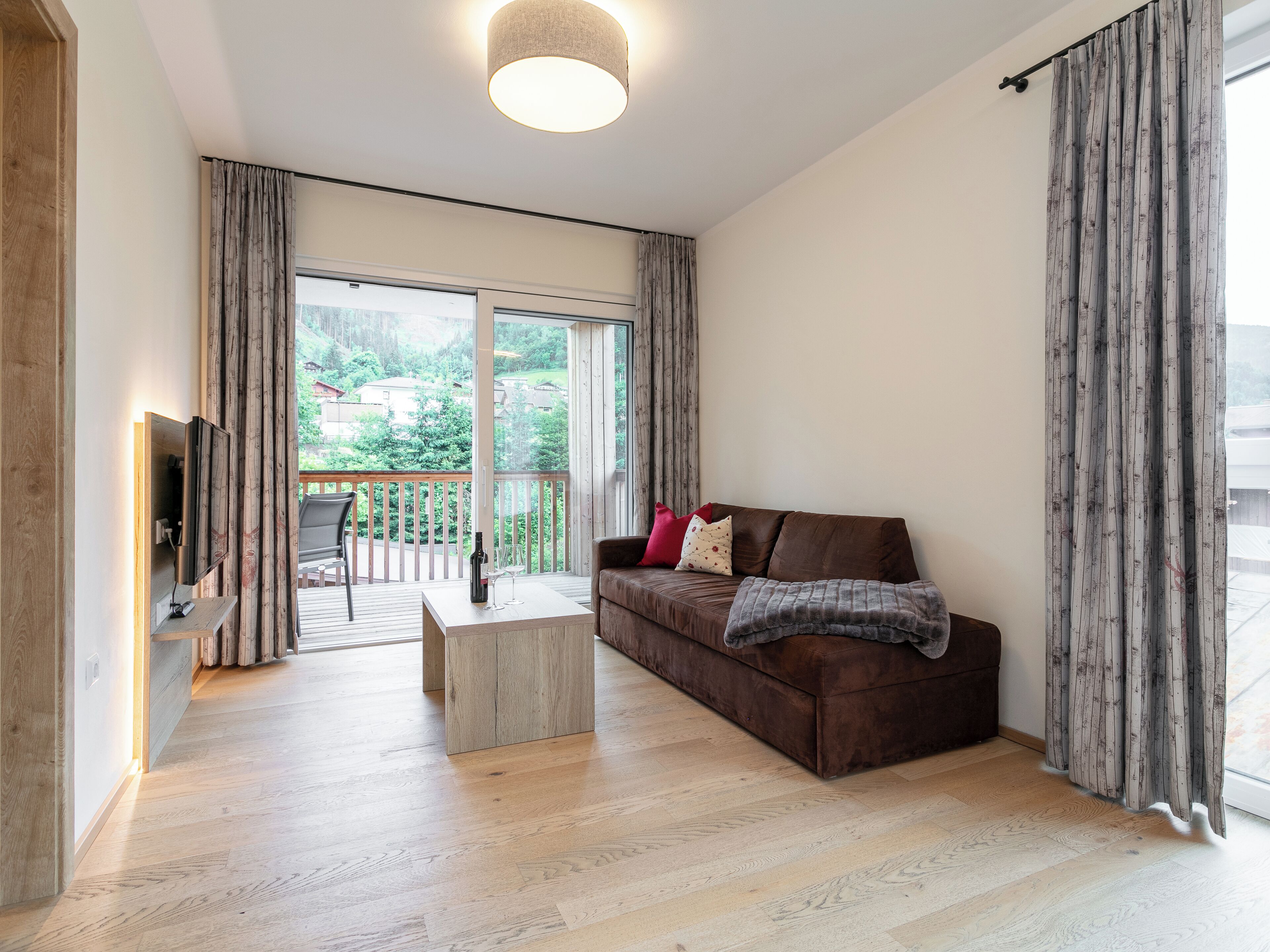 Ein geräumiges Wohnzimmer mit Holzboden, einem braunen Sofa, einem Couchtisch und einem an der Wand montierten Fernseher.