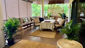 Un espace intérieur moderne comprenant un canapé, une table et des chaises, agrémenté de plantes en pot et doté de grandes fenêtres offrant une vue sur la verdure.