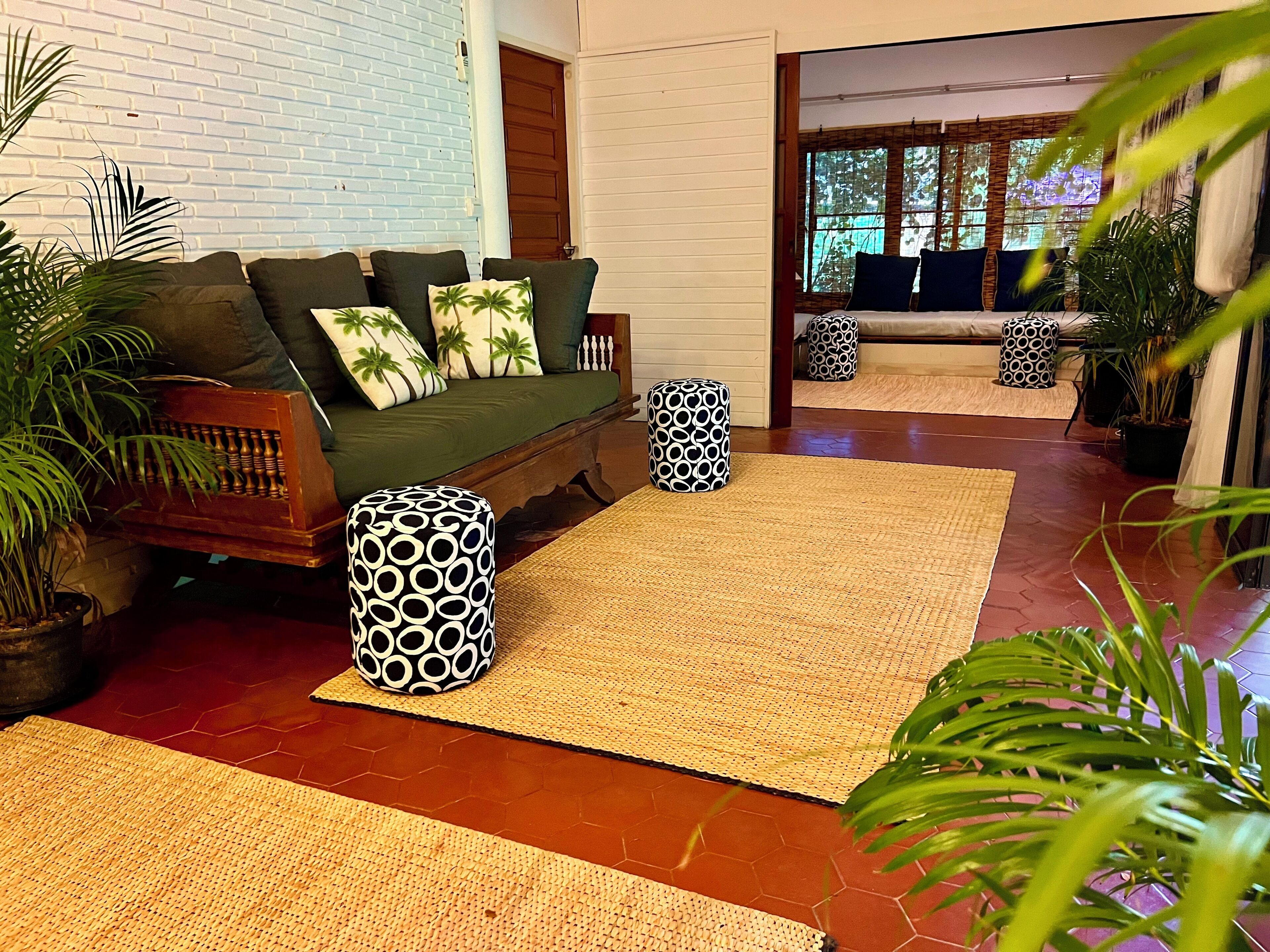 A modern living room with a sofa, patterned ottomans, and potted plants.