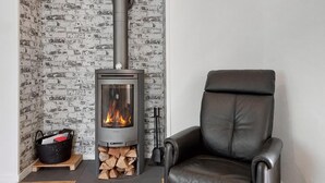 A room with a wood-burning stove, a black leather chair, and a brick-patterned wall. - Awesome home in Vittsjö with WiFi (Vittsjö)