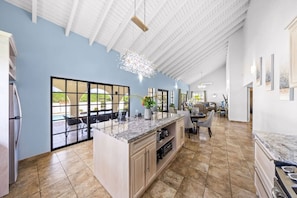 A spacious kitchen with a large island, a dining area with chairs, and a view through a glass door to an outdoor area.