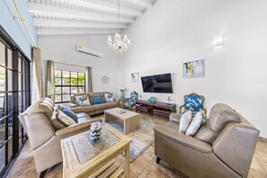 A spacious living room with a large TV, comfortable seating, and a chandelier.