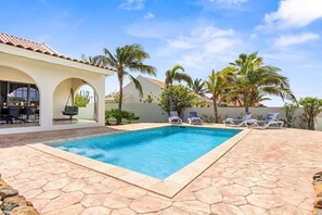 A swimming pool with lounge chairs, a patio area, and palm trees.