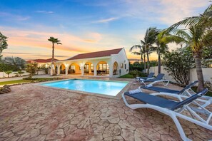 A pool area with lounge chairs, a stone patio, and a building with arched windows.