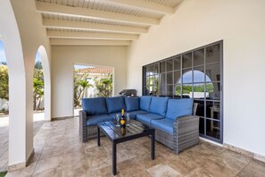 An outdoor patio area with a blue sofa, a glass table with a bottle, and a view of the outdoors.