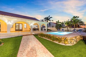 Une propriété résidentielle dotée d’une piscine, d’un patio couvert avec coin salon et d’une pelouse bien entretenue.